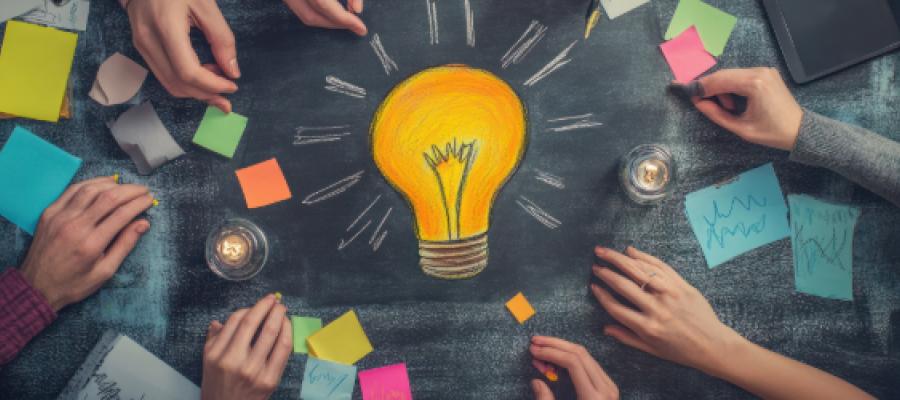 Lightbulb drawn in centre of chalkboard with post it notes and hands surrounding it